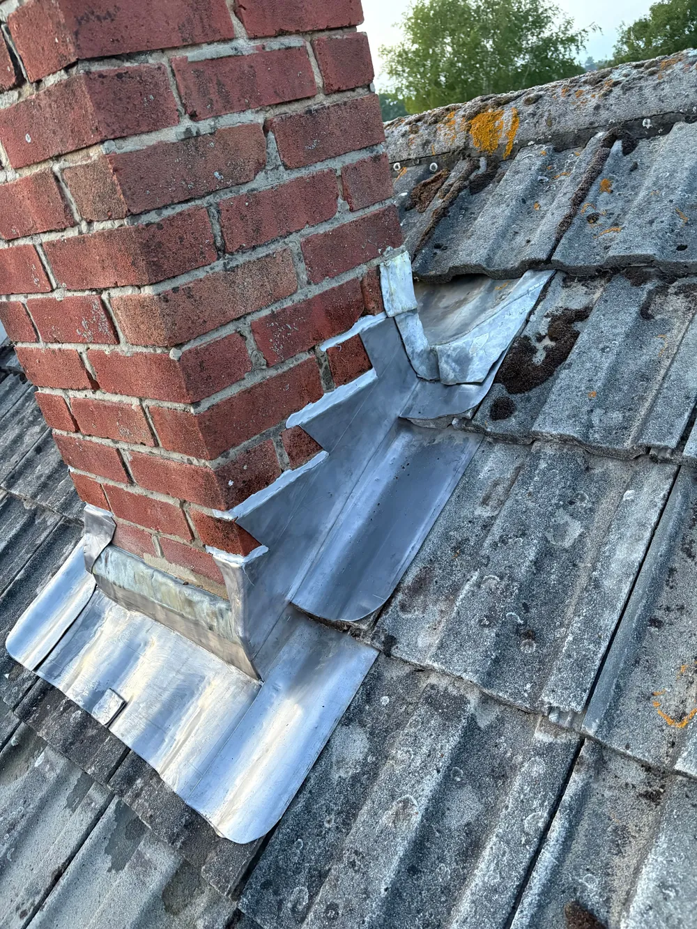 Before: split and oxidised lead apron at the base of a brick chimney with moss on the surrounding tiles