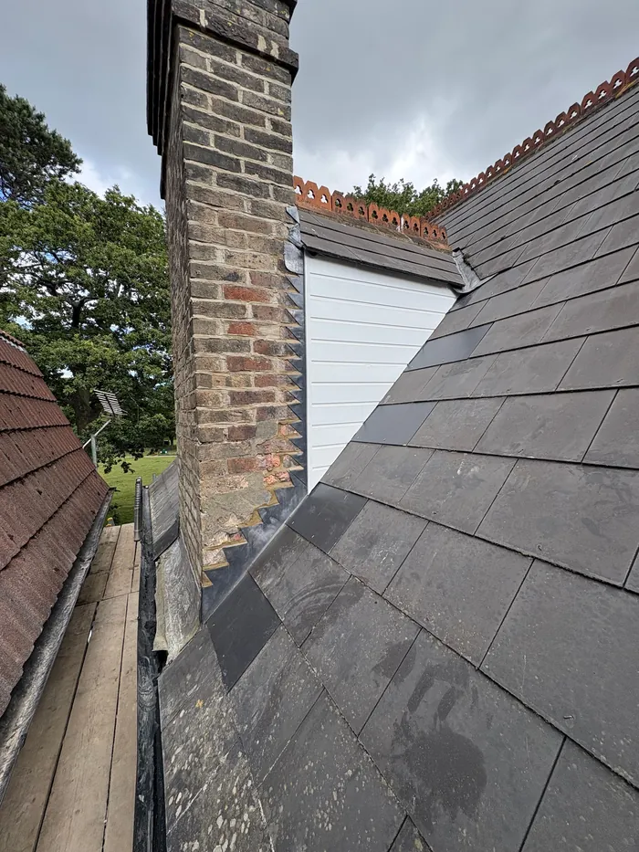 Re-slated roof section beside a brick chimney with new white cladding on the gable