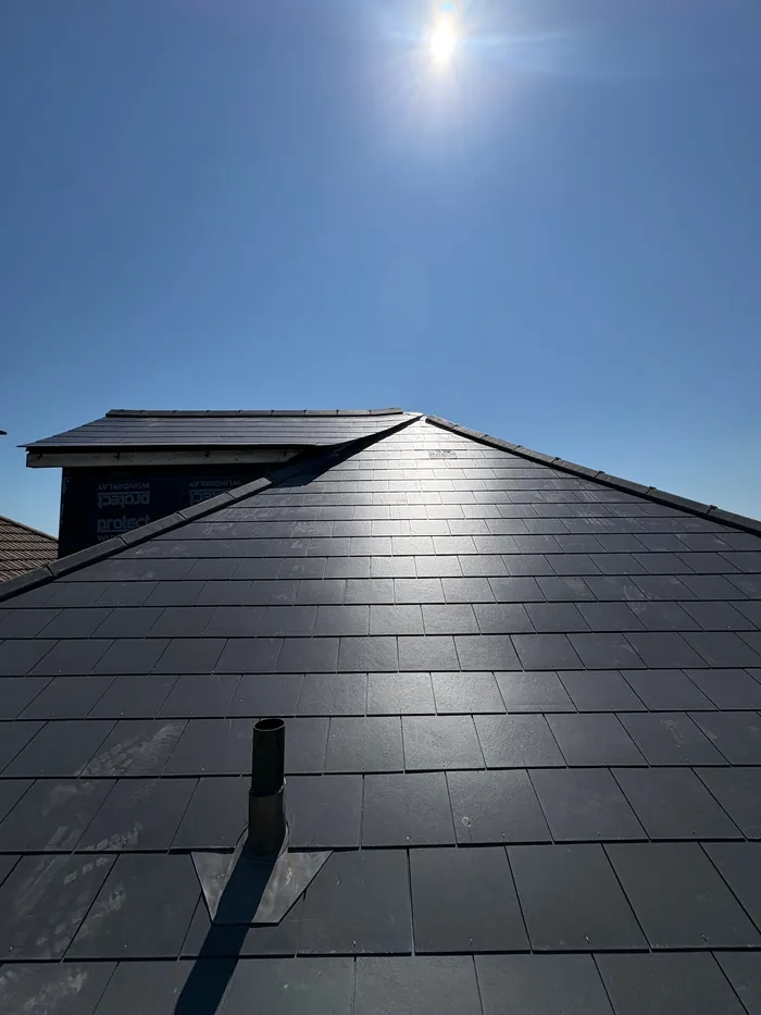 New Jutland Graphite slate roof with a lead-flashed vent pipe and a dormer behind, under a clear sunny sky