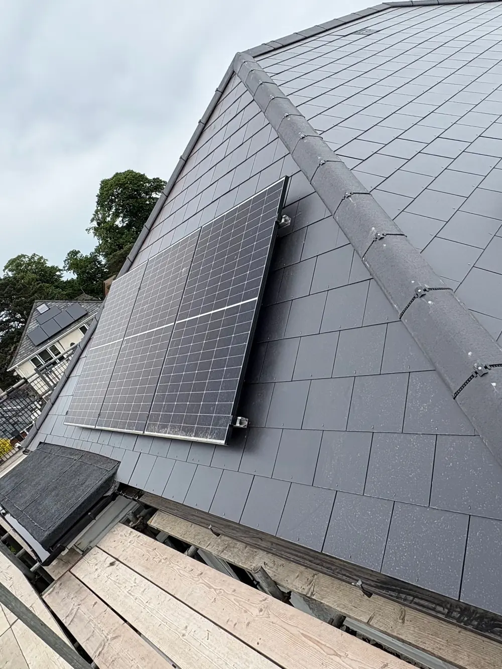 After: the same roof re-slated in Jutland man-made slate, with a grey Modern ridge running up the hip and the solar panels refitted onto the new slates