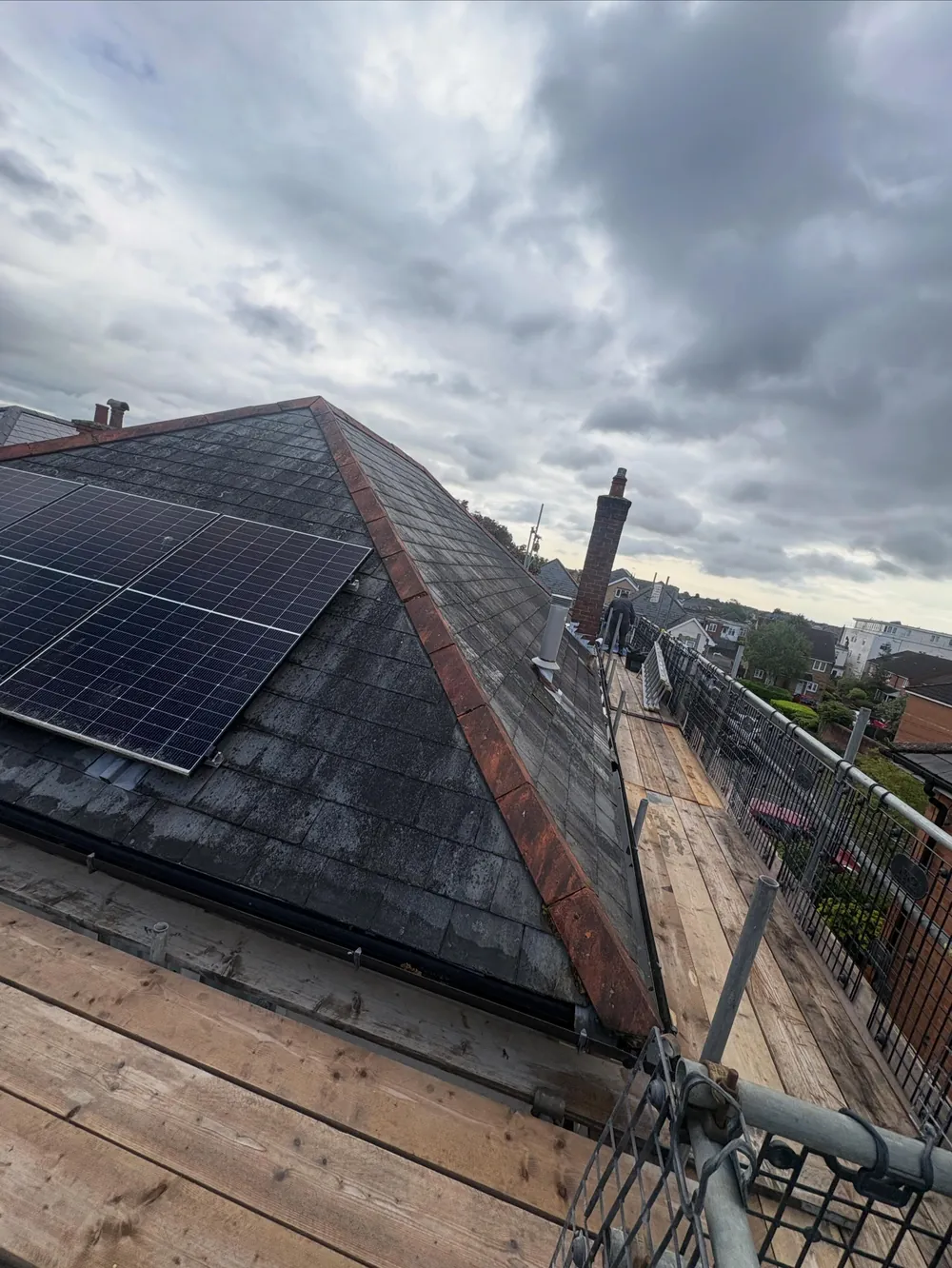 Before: old natural slate hip roof with solar panels and a chimney, under grey skies