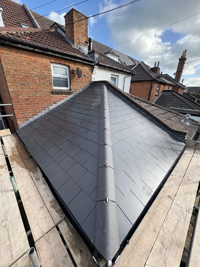 Finished hipped lean-to roof in man-made slate with new lead against the brick wall, seen from the scaffold