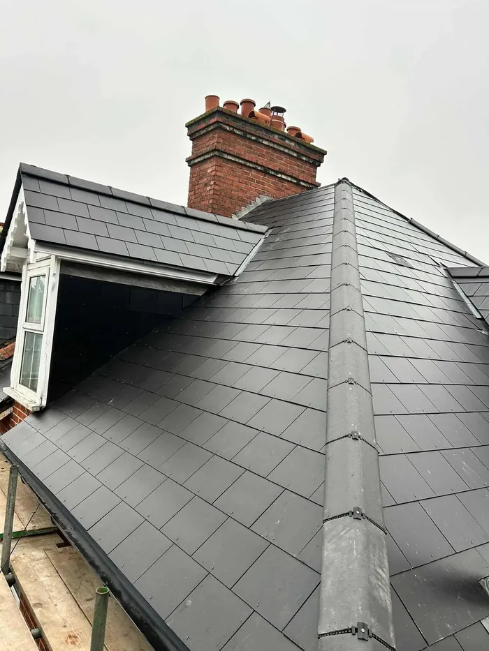 Finished two-hip re-roof in Swanage in Jutland blue-black slate with grey Modern ridges, dormer and brick chimney