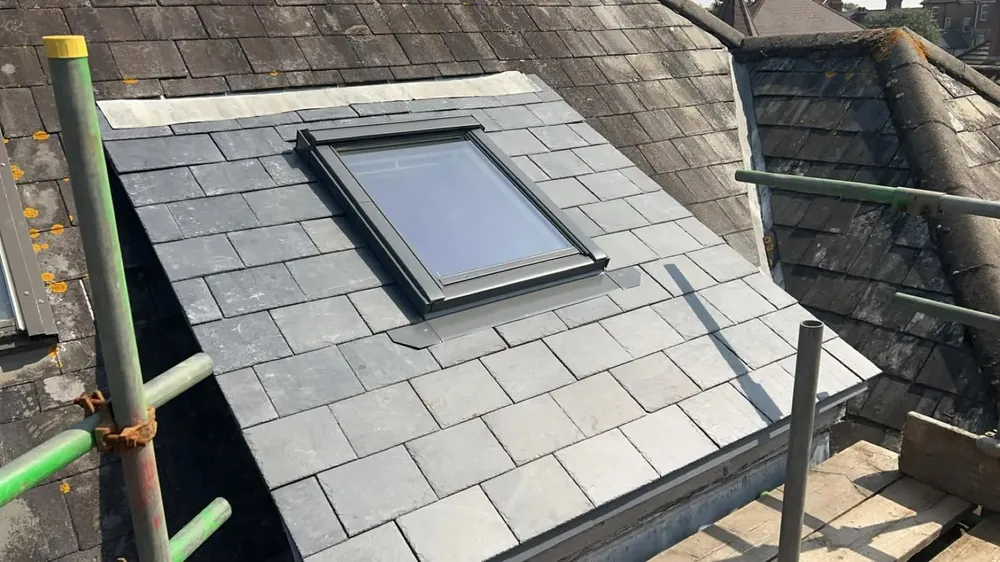 New Velux roof window fitted into a freshly re-slated roof section, seen from the scaffold